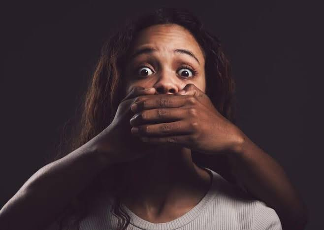 Young woman with both hands over her mouth against a dark background