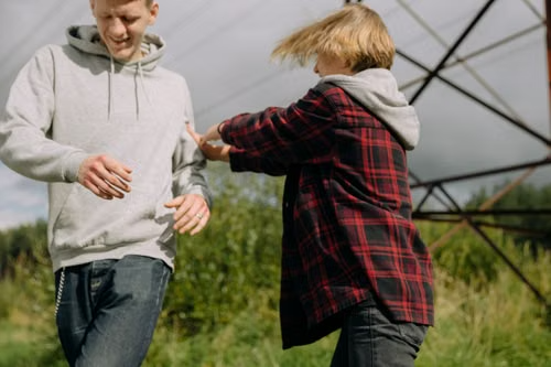 A father and his teenage son laughing and playfully sparring outdoors in a grassy field