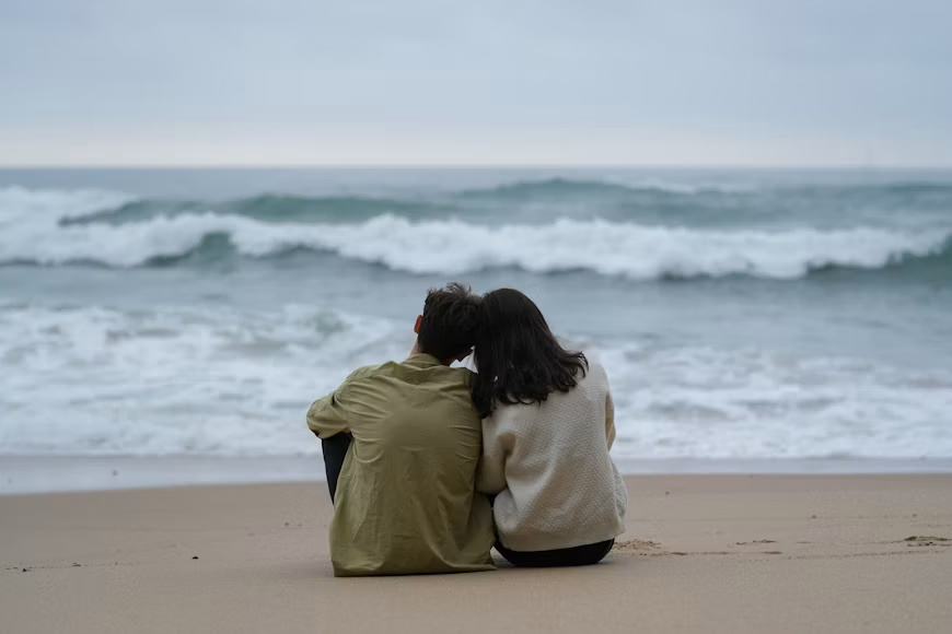 Young couple sitting side by side on a beach watching the waves, illustrating California close-in-age relationships
