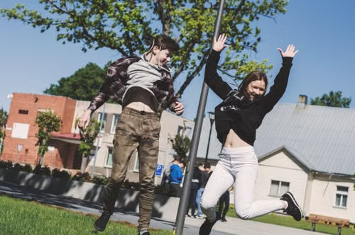 Two teenagers jumping and laughing outside a school on a bright spring day