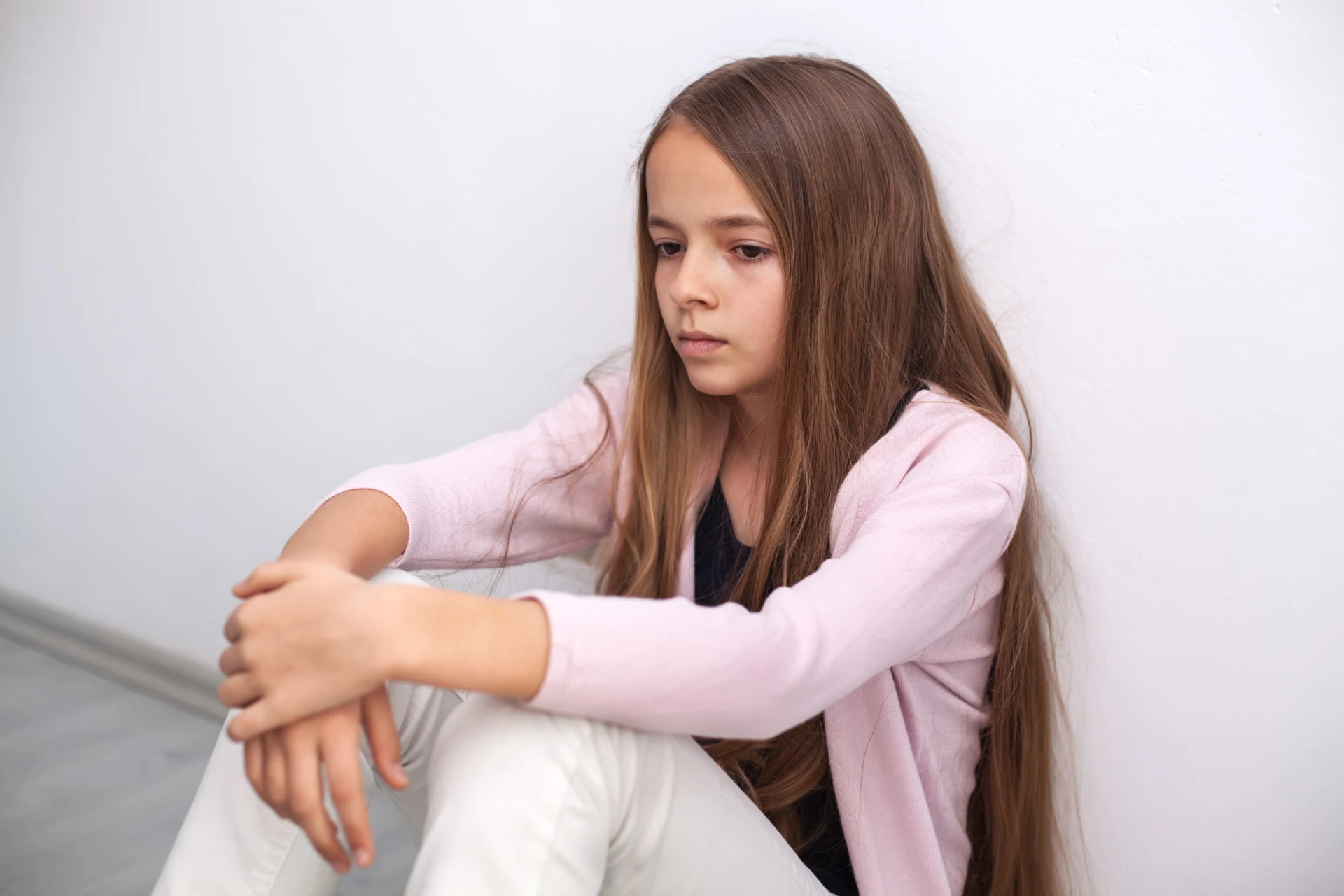 Young girl sitting alone against a plain wall, representing the protective purpose behind age of consent statutes