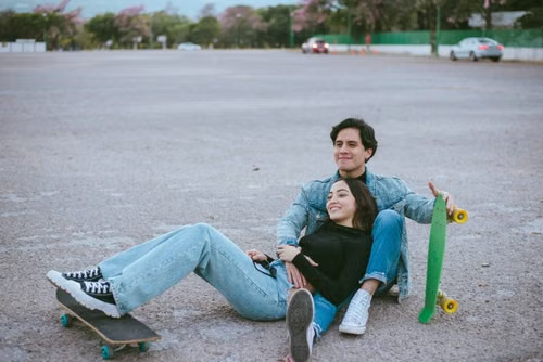 Two teenagers sitting on skateboards at an empty lot at dusk, relaxed and casual