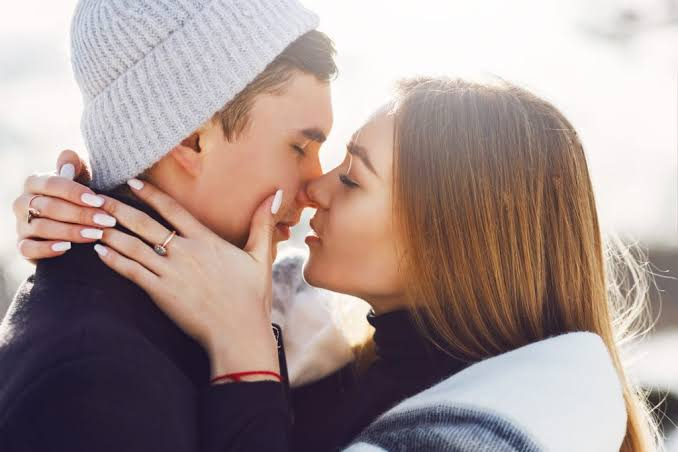 Teenage couple in winter clothing leaning in close to each other outdoors