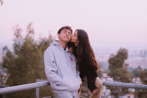 Teen couple sitting on a hillside railing at dusk, illustrating Kansas unlawful voluntary sexual relations rules