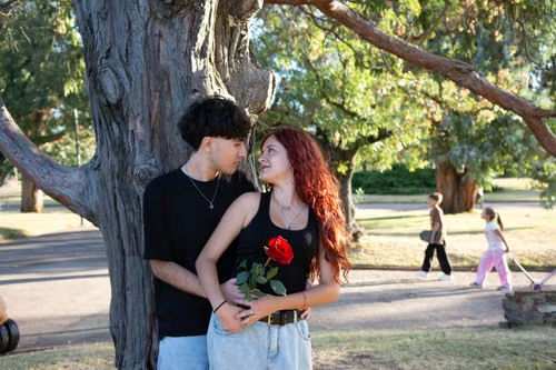 Teen couple standing under a park tree holding a red rose, illustrating Kentucky's offender-age floors