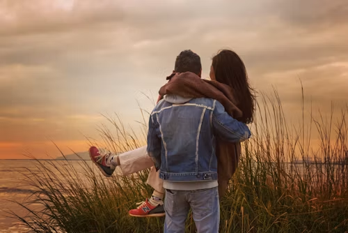 Young man lifting his partner near tall grass by the shore at sunset, illustrating Florida's close-in-age provisions