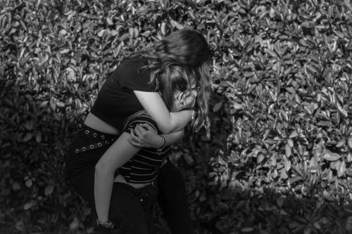 Black and white photo of a teen couple embracing beside a hedge, illustrating Wyoming's stacked age conditions