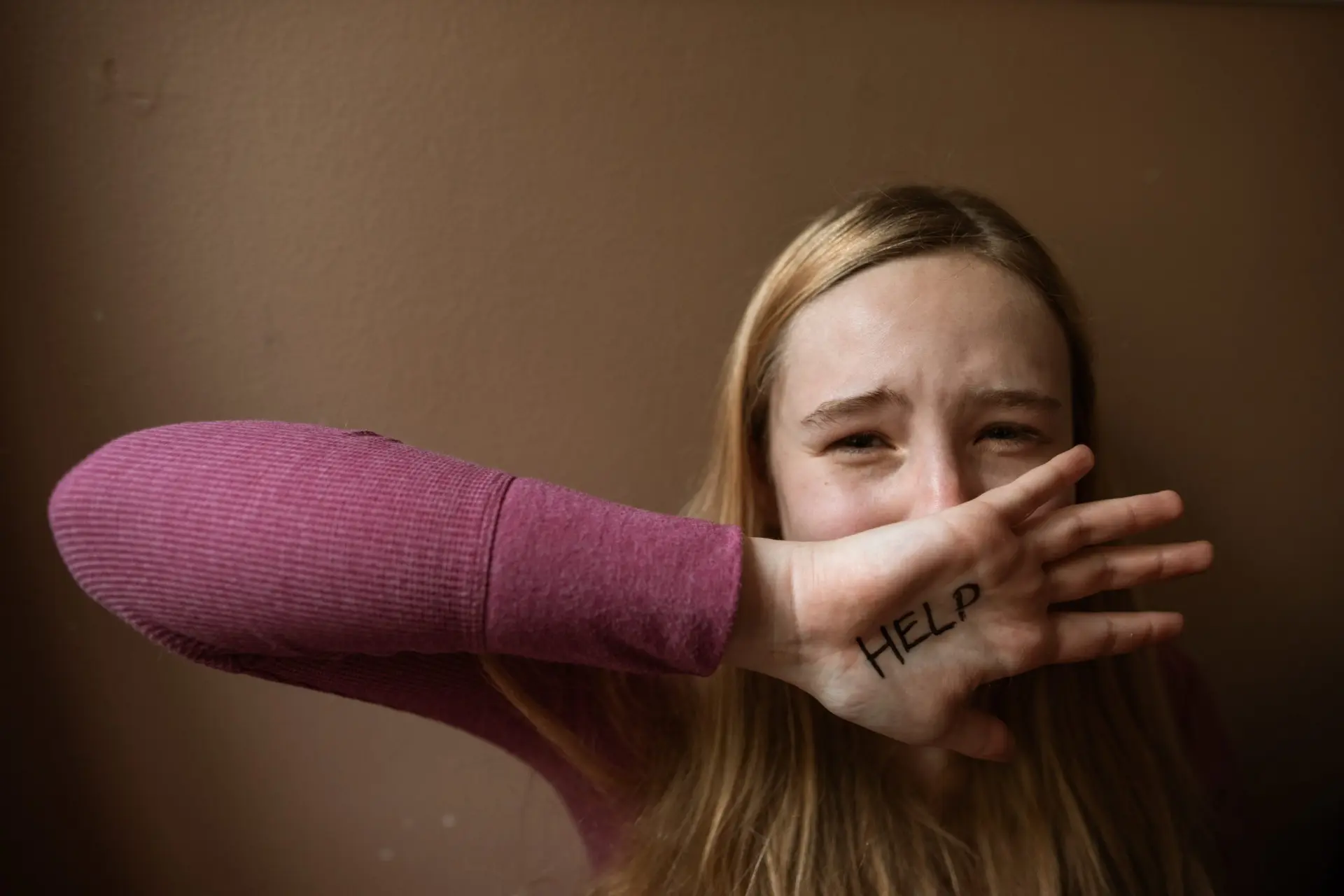 Teenage girl covering her mouth with the word HELP written on her hand
