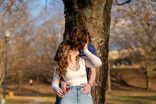 Teen couple standing close by a tree in a sunlit park, illustrating Maine's paired age thresholds