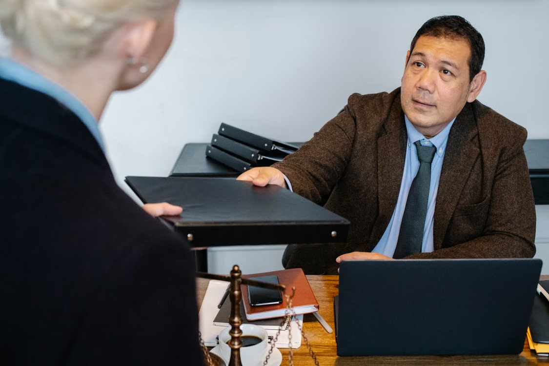 Defense attorney handing a case file across a desk to a client during a consultation